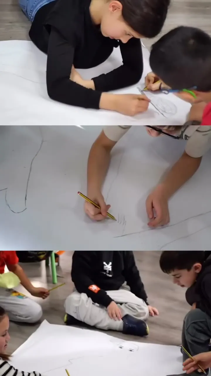 Ikasleak arkatzez marrazten paper handi baten gainean, gelako lurrean