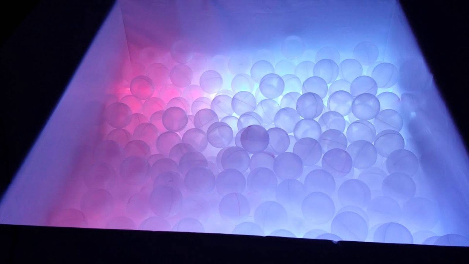 La piscina de bolas real del aula Snoezelen: decenas de bolas blancas translúcidas encendidas desde dentro con luz rosa y azul.