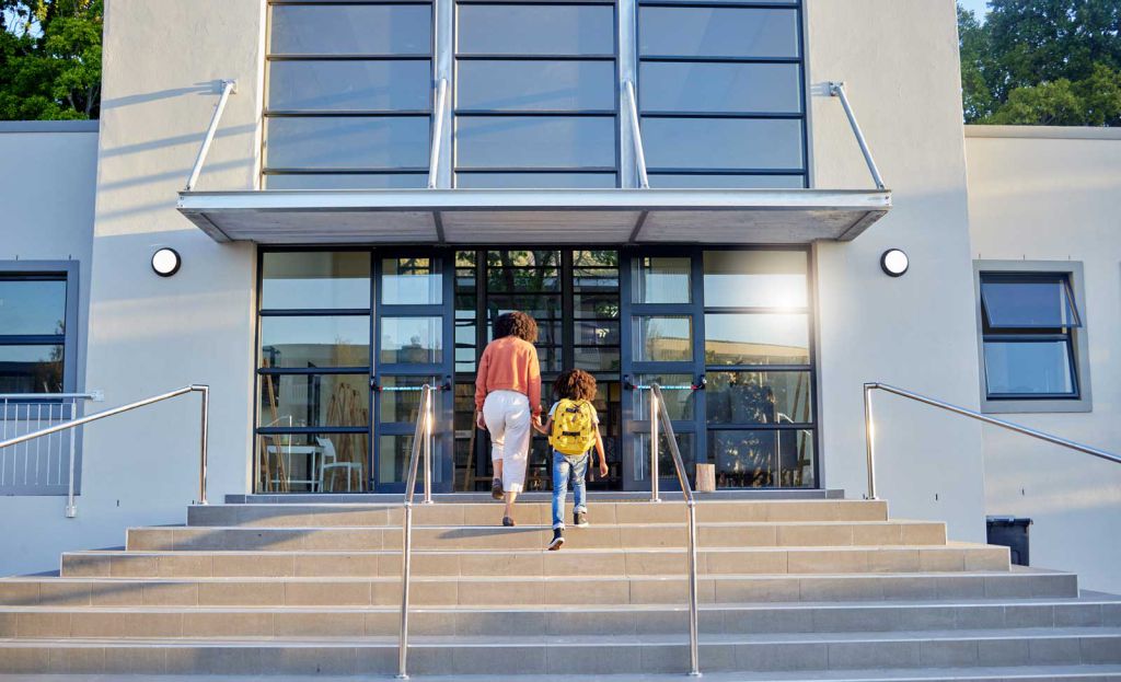 Una madre y su hija subiendo las escaleras de entrada del colegio