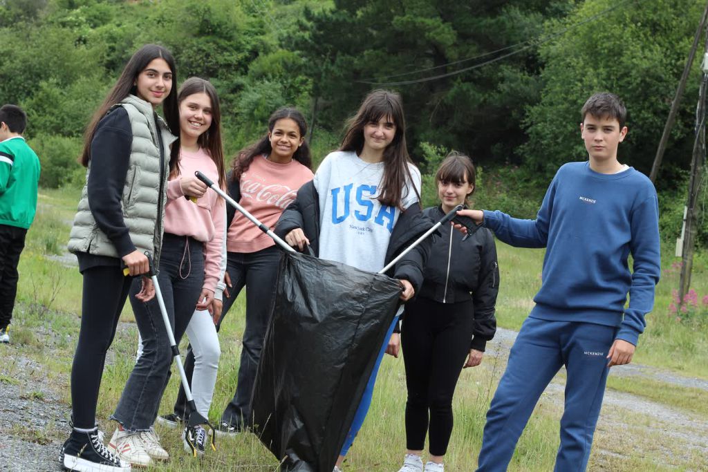 Seis alumnos y alumnas de San Felix, con pinzas de recogida y una bolsa grande, en un camino del entorno del municipio