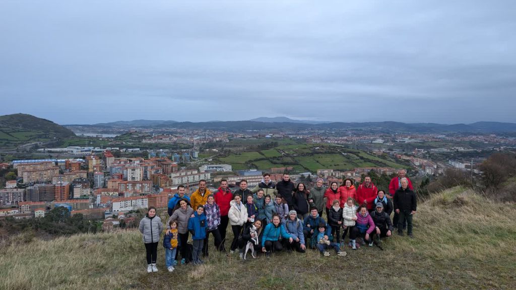 Grupo numeroso de alumnado y familias de San Felix posa en lo alto de un monte, con el valle y la ría al fondo