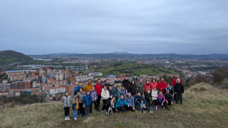 Grupo numeroso de alumnado y familias de San Felix posa en lo alto de un monte, con el valle y la ría al fondo