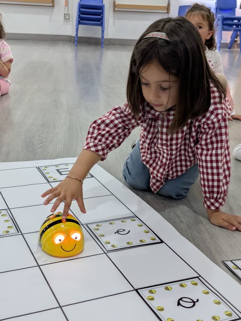 Una niña de infantil coloca un robot con forma de abeja sobre un tapete de cuadrículas